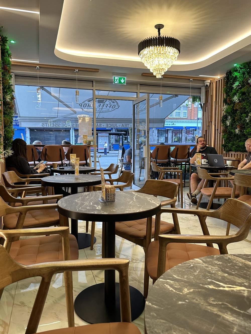 Wooden chairs and round marble tables in the seating area, with the glazed shopfront behind.