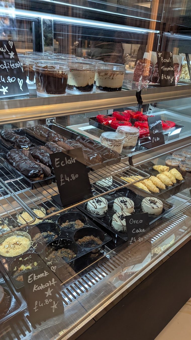 A row of cakes and eclairs in the patisserie display, cropped away from the price labels.